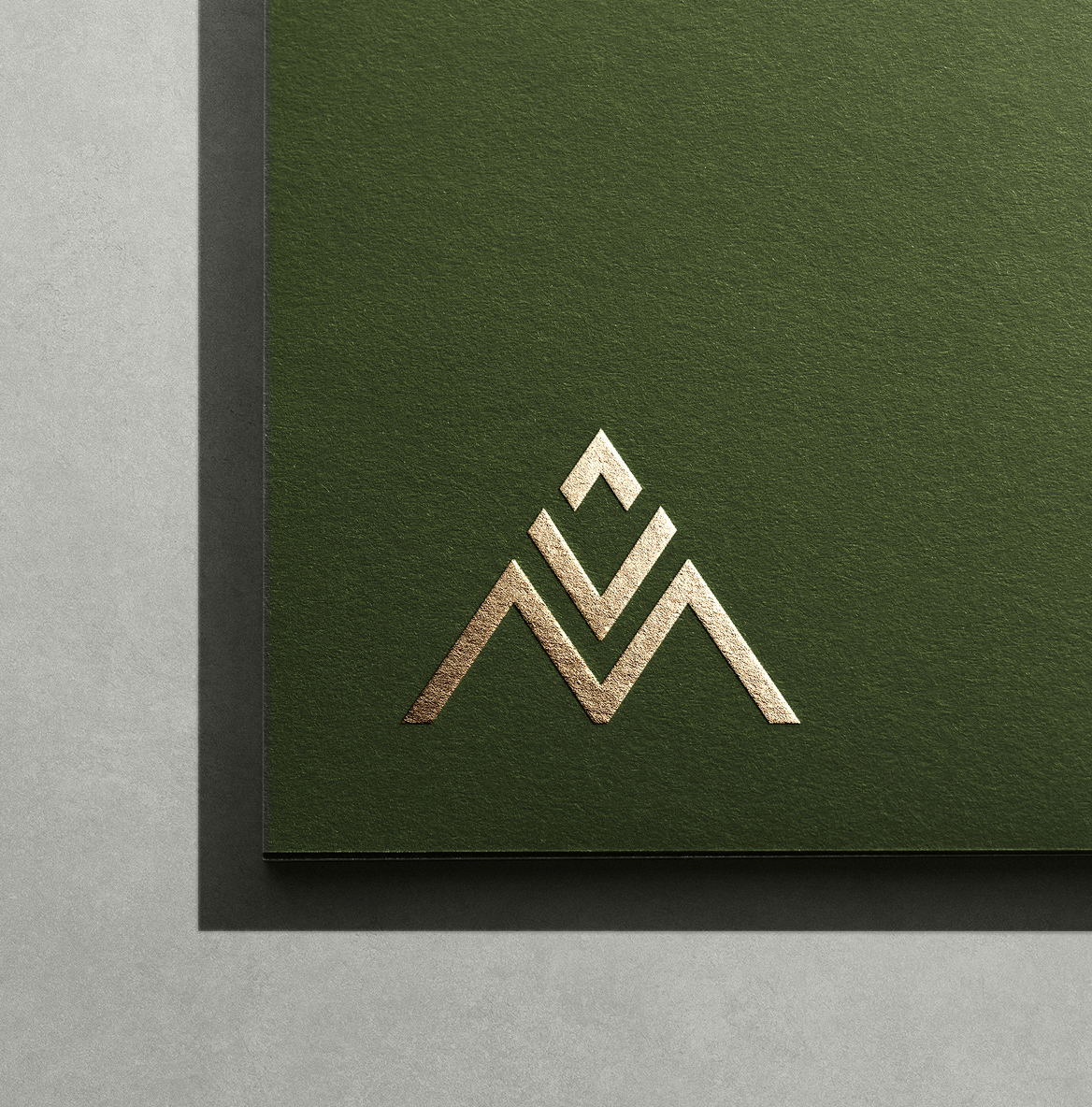 A green textured card displays a gold foil geometric logo resembling a stylized mountain. The design conveys a sense of elegance and modernity.