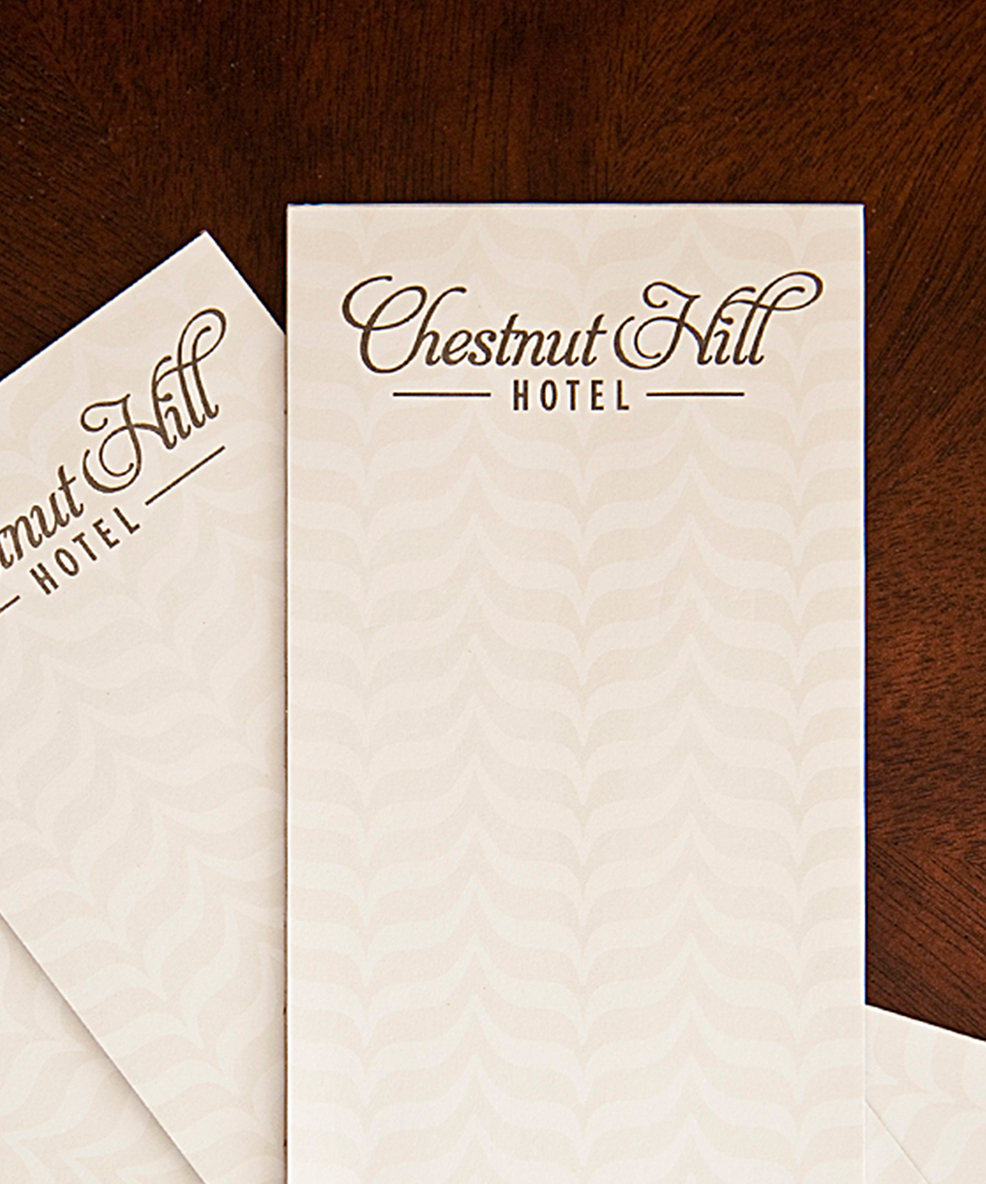 Elegant stationery from Chestnut Hill Hotel, featuring a subtle leaf pattern on cream paper, resting on a wooden surface.