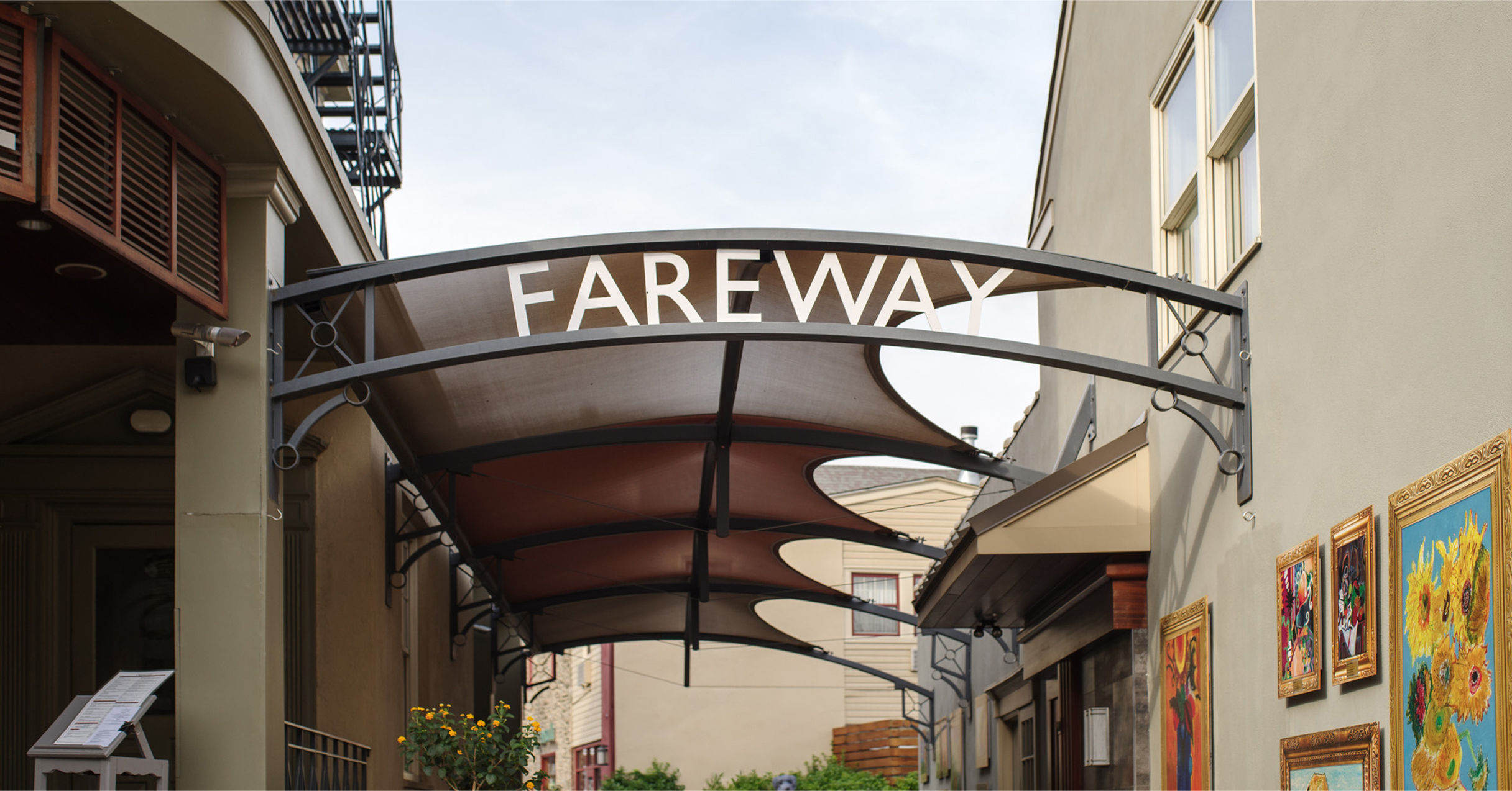 Covered walkway with 'Fareway' sign in an alley. Art-covered walls and nearby plants add a vibrant, inviting atmosphere on a clear day.