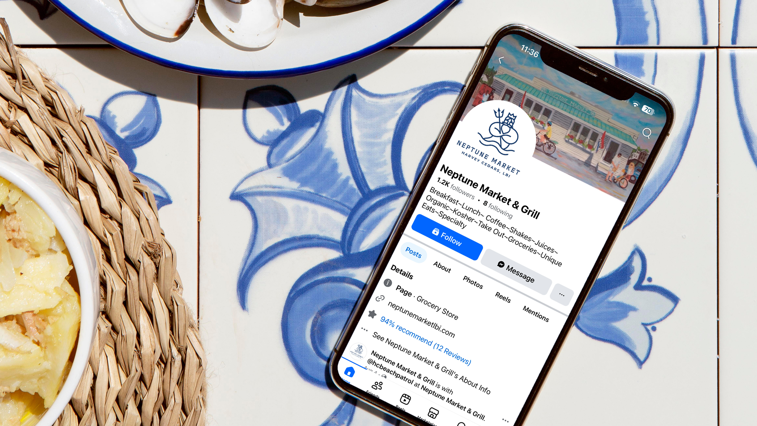 Smartphone displaying Neptune Market & Grill's profile on social media, placed on a blue floral tiled table. Nearby, dishes with food evoke a casual dining ambiance.