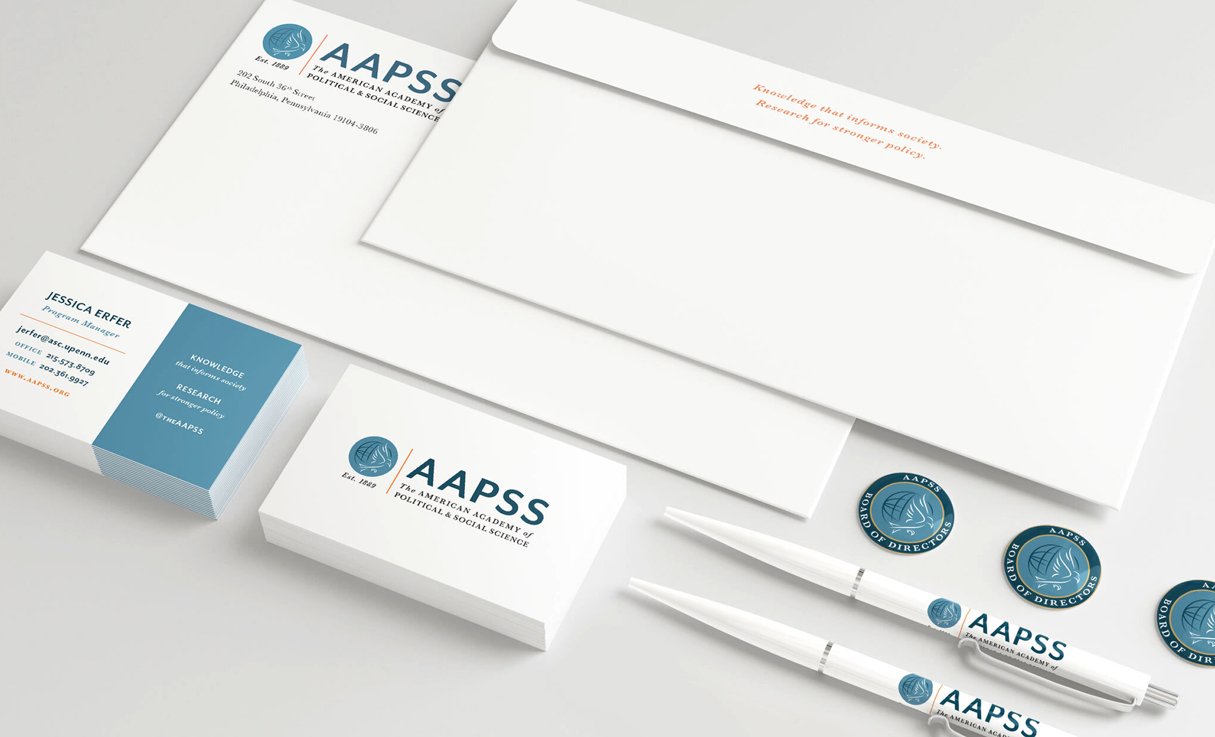 A stationery set with AAPSS branding includes business cards, envelopes, pens, and badges. The design is sleek and professional, using white, blue, and orange accents.