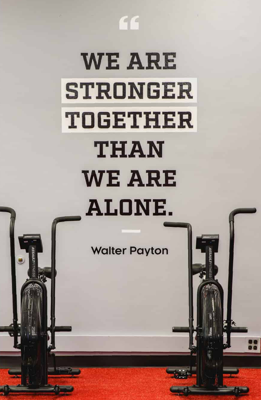 FitU-Bikes Gym room with red carpet and two exercise bikes in front of a wall quote: "We are stronger together than we are alone." - Walter Payton. Motivational tone.