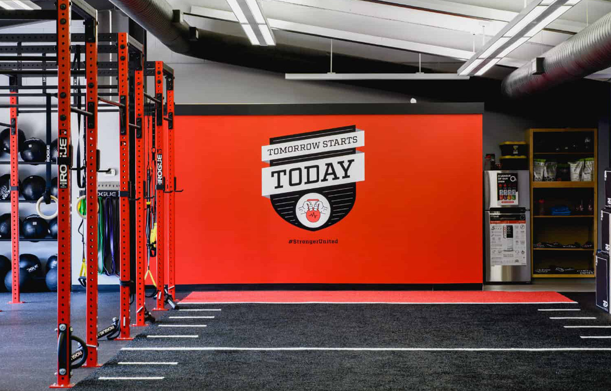 FitU-Gym A modern gym interior with vibrant red walls displays the motivational text "Tomorrow Starts Today." Red exercise racks line the left, and equipment is neatly organized.
