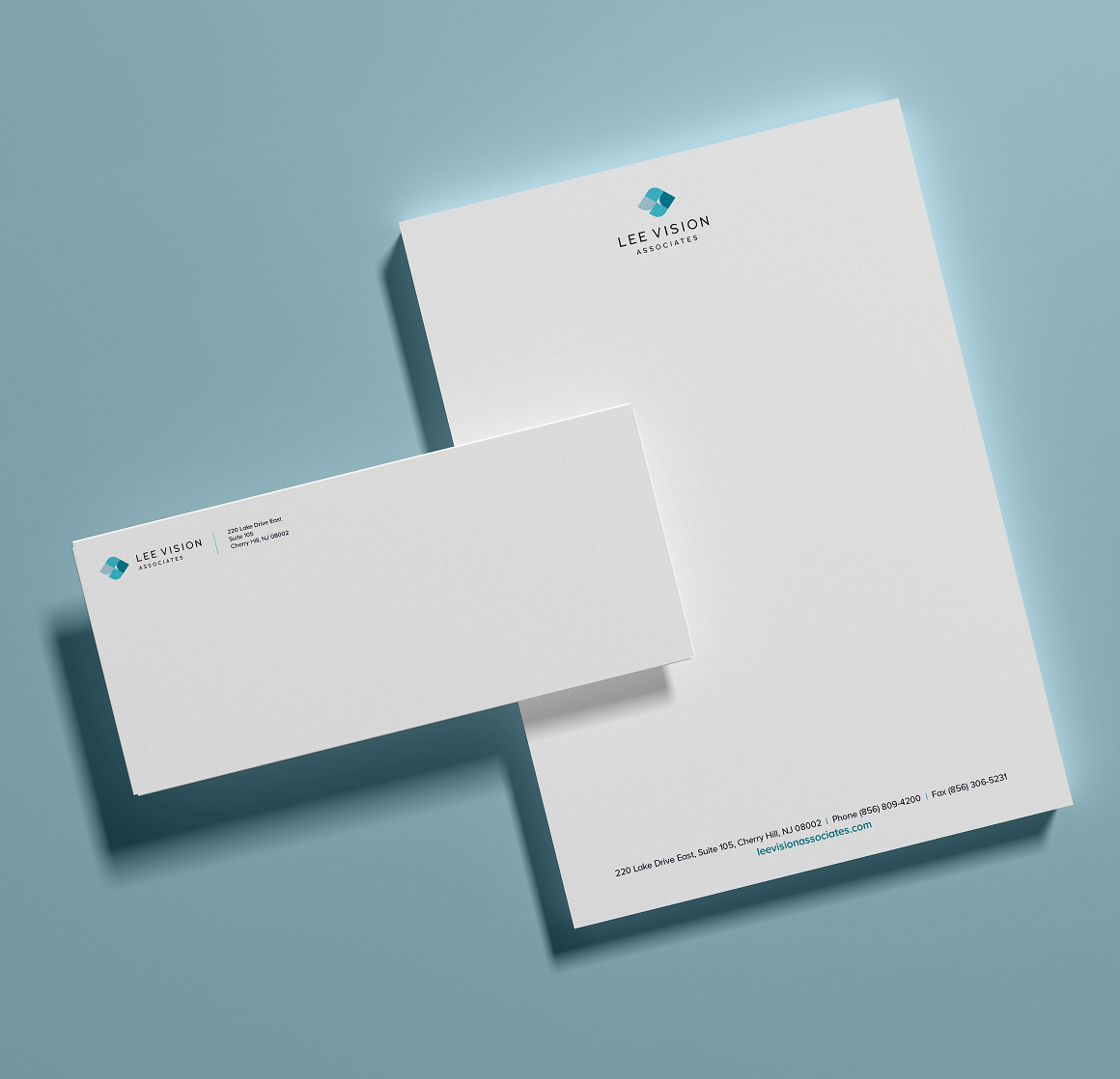 A modern stationery set for Lee Vision Associates with a white letterhead and envelope on a light blue background. Both feature a simple blue logo and text, conveying professionalism.