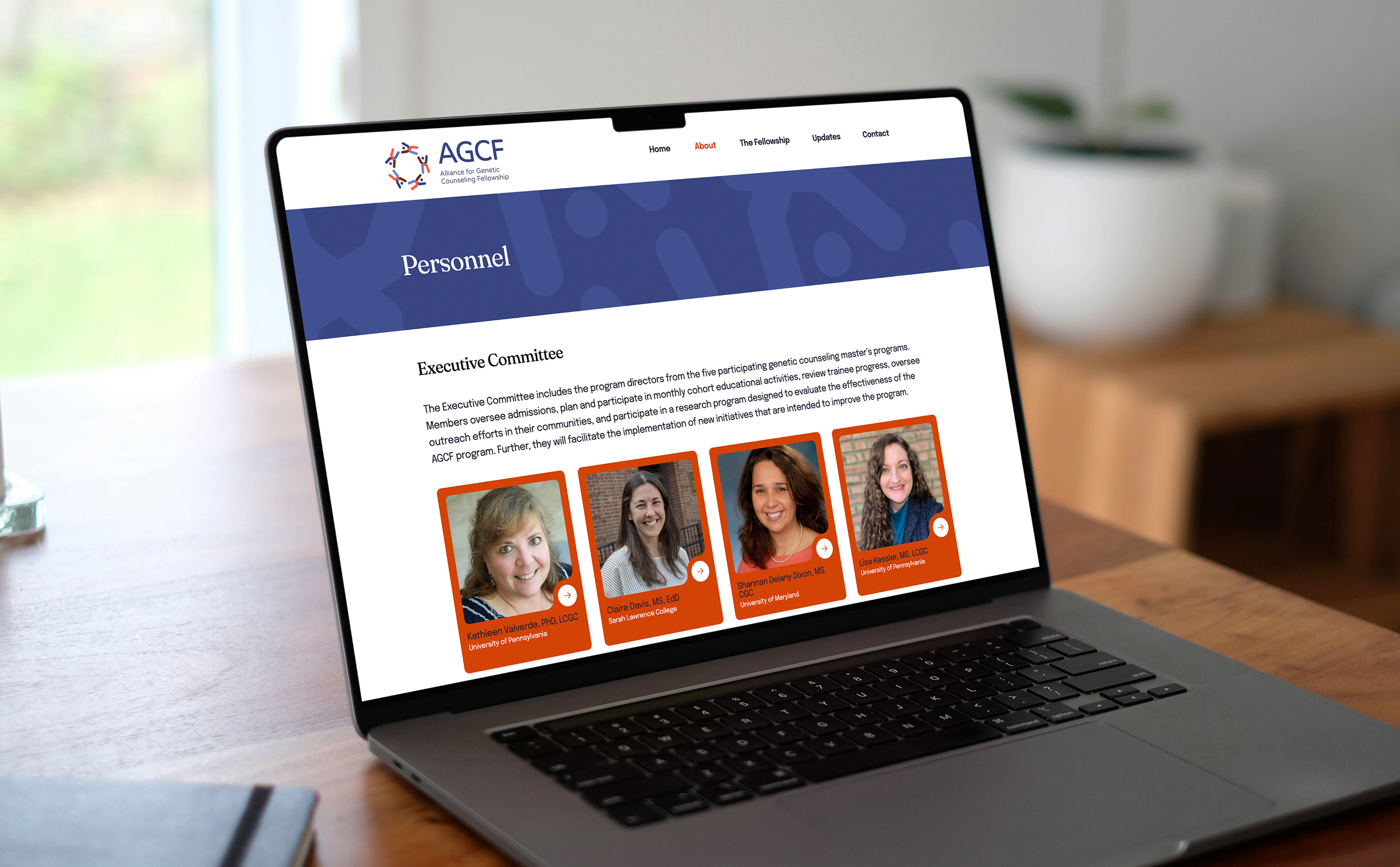 Laptop on a wooden table displaying the AGCF website, showcasing portraits of four women within red boxes in a "Personnel" section.