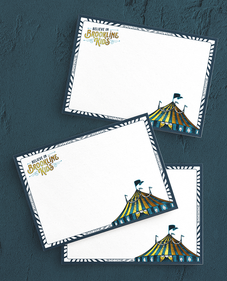 Three white notecards with bold navy borders overlap on a textured blue surface. At the top of the notecards reads "Believe in Brookline Kids" in blue and gold, with a colorful circus tent illustration at the bottom.