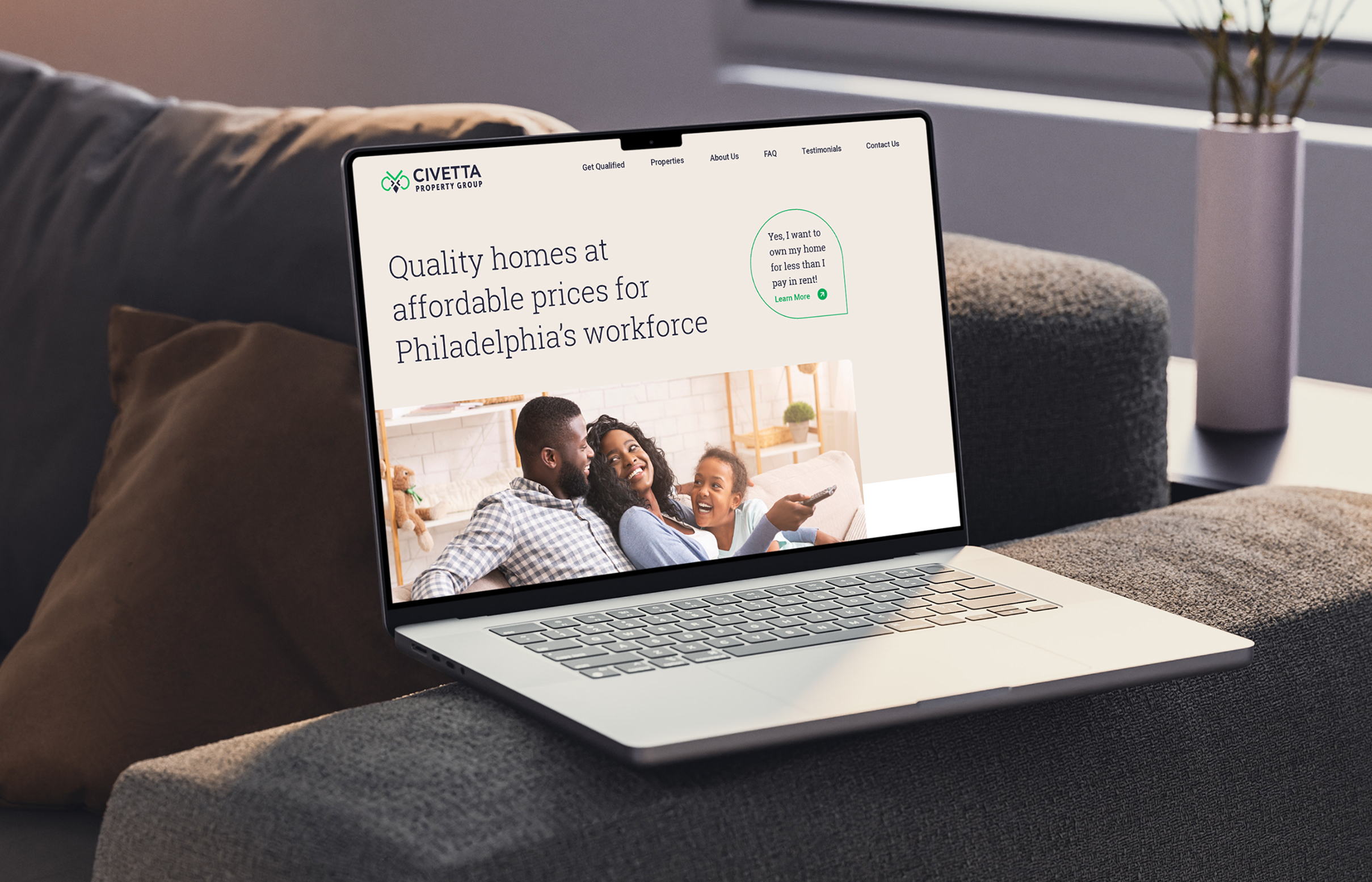 Civetta-Homepage A laptop displaying the Civetta Property Group website is on a couch. The screen shows a headline about affordable homes for Philadelphia's workforce, with an image of a happy family.