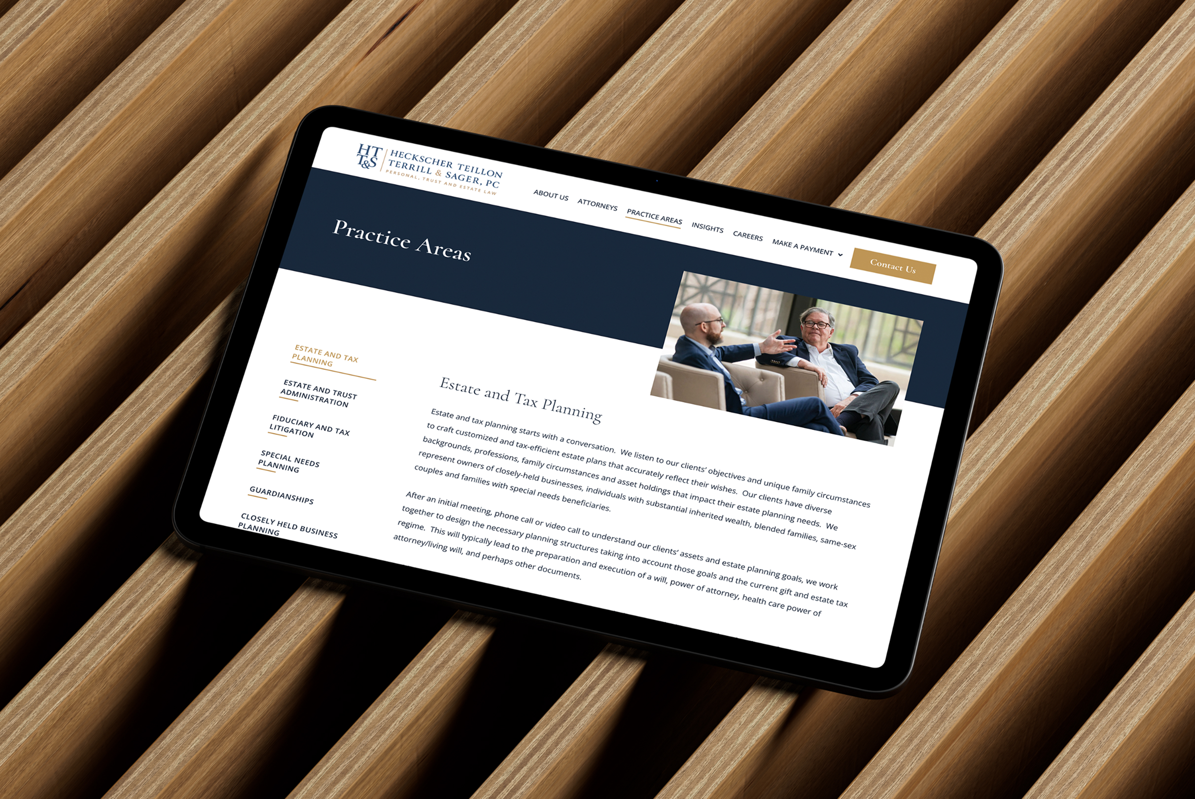 Tablet displaying the "Practice Areas" page on the website for HTT&S. The page discusses estate and tax planning, featuring a photo of two men in suits conversing. The tablet sits on a textured wooden surface.