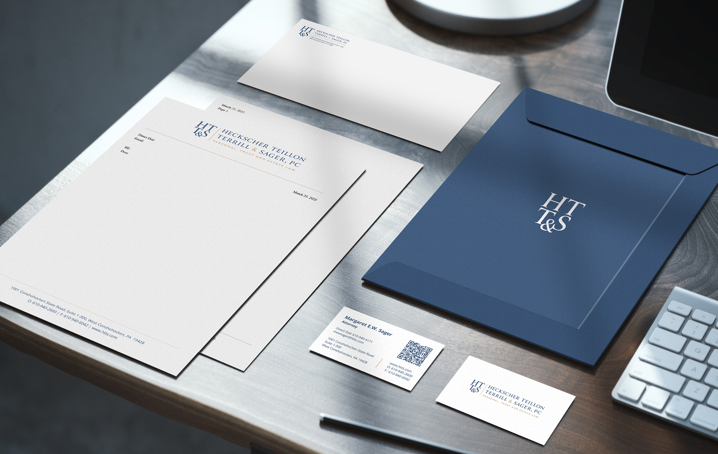 Stationery suite for HTT&S featuring a blue envelope, letterhead, and business cards. Each piece sits on a wooden desk by a keyboard. Professional and sleek stationery setup.