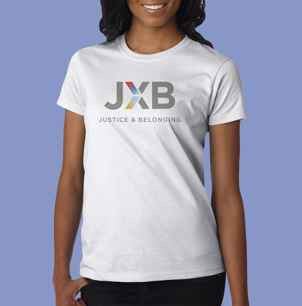 A woman wearing a white T-shirt with the JXB logo. The logo has the letters "JXB" with a colorful "X" in red, blue, and yellow hues. Below, the text reads "Justice & Belonging."