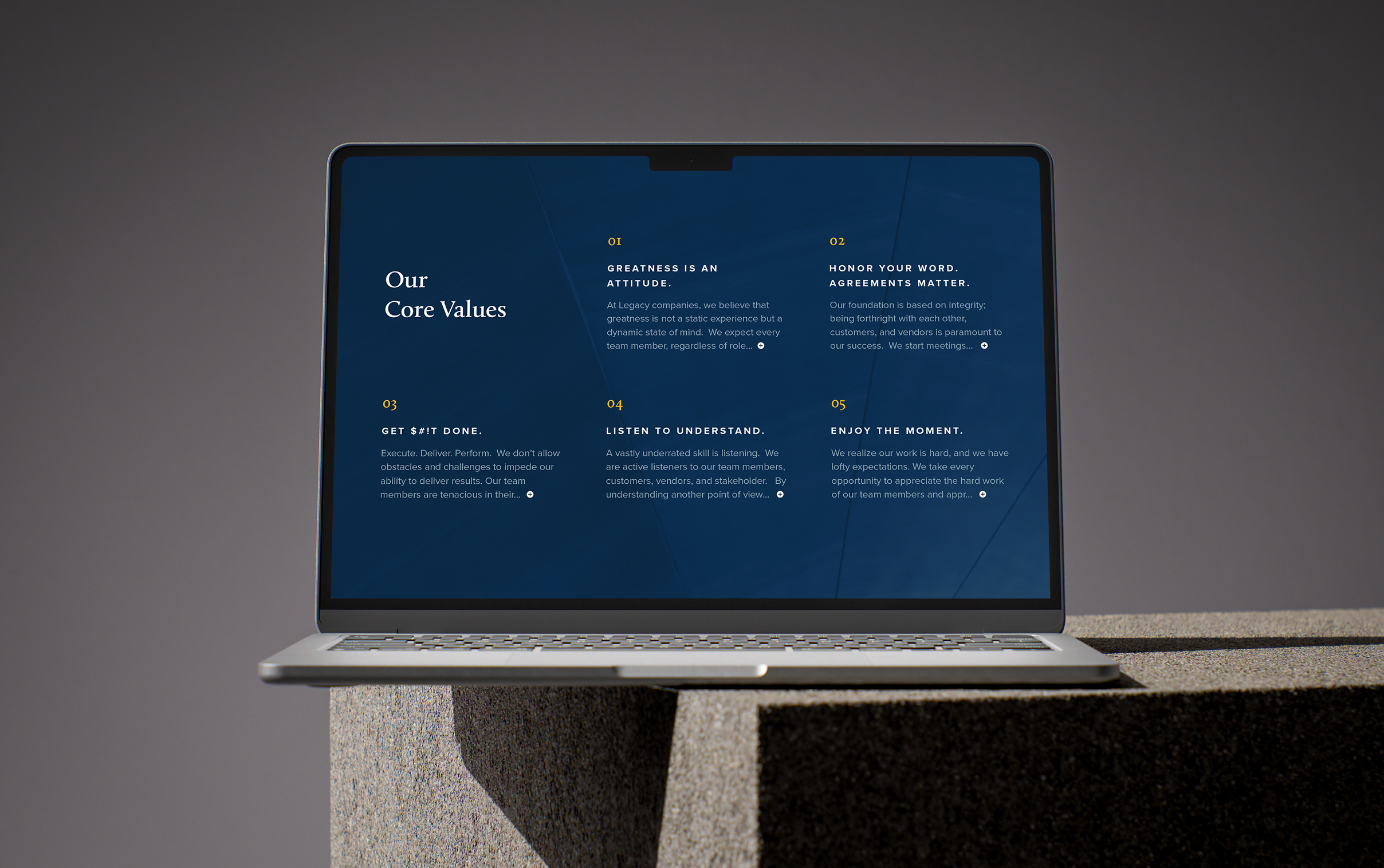 Legacy-Laptop A laptop displaying a page from the Legacy Companies website with text titled "Our Core Values" on a dark blue screen. The laptop rests on a concrete surface, conveying a professional, modern tone.