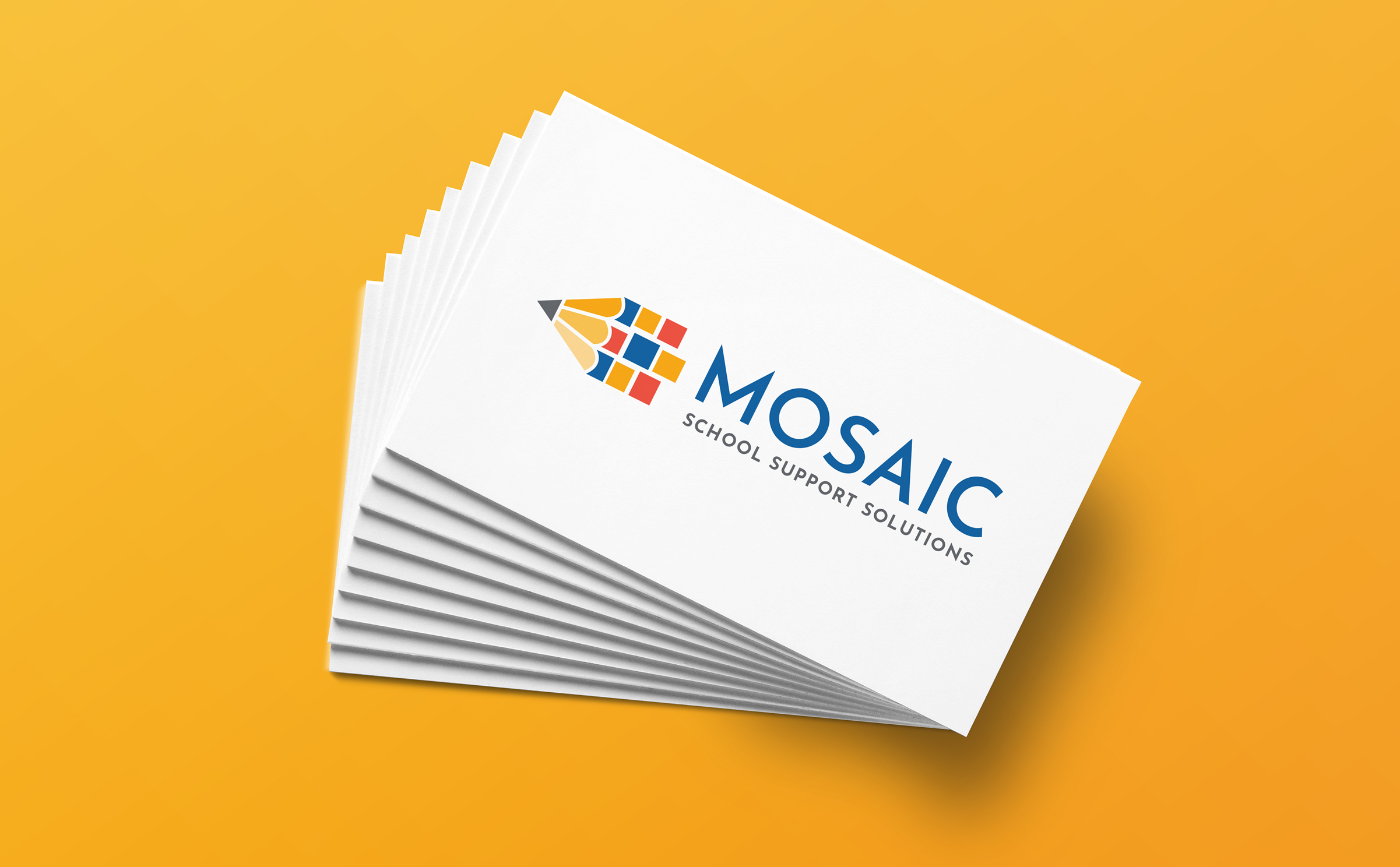 A stack of business cards on a yellow background. The cards feature a logo. The logo has a bright geometric pencil on the left with blue, red, and yellow. The word “Mosaic” appears to the right in large blue letters. Underneath is the tagline “School Support Solutions.”