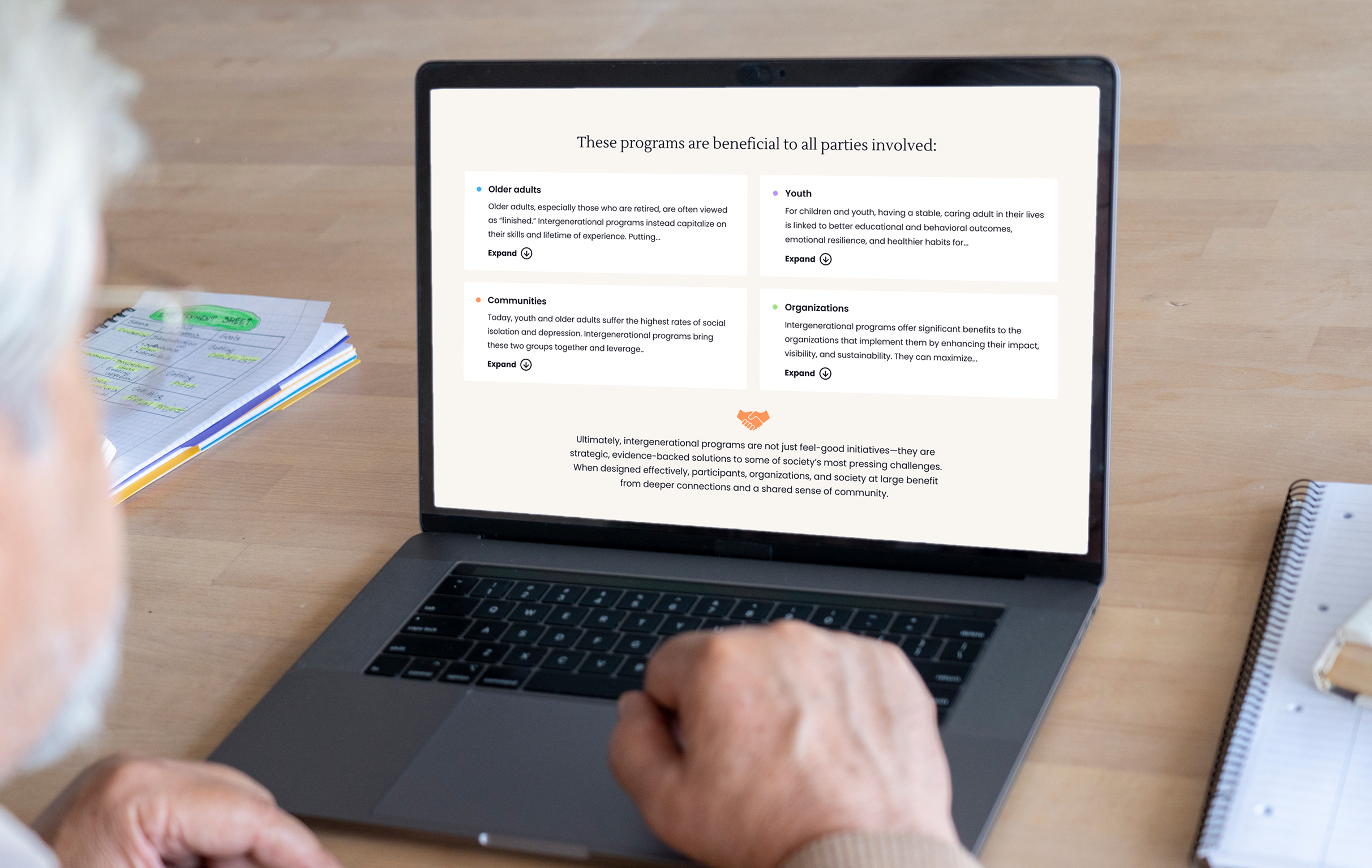 A person views a laptop displaying a page from The Eisner Foundation website with text reading "These programs are beneficial to all parties involved." Sections on older adults, youth, communities, and organizations listed underneath.