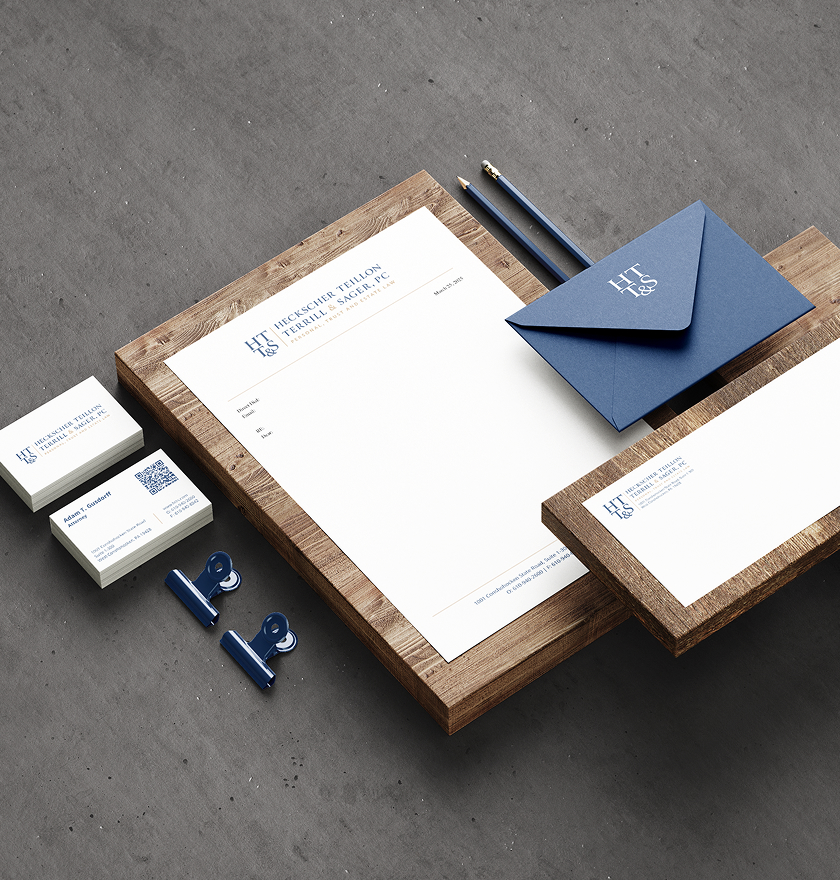 HTTS-Stationery Navy-and-white business stationery featuring a letterhead, envelope, cards, pencils, and clips arranged on wooden trays against gray stone.